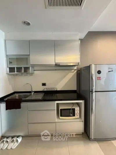 Modern kitchen with sleek cabinetry, stainless steel fridge, and built-in microwave in a compact layout.