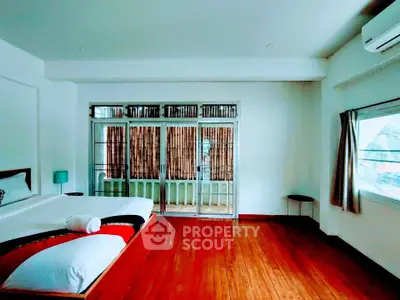 Spacious bedroom with wooden flooring and large windows for natural light.