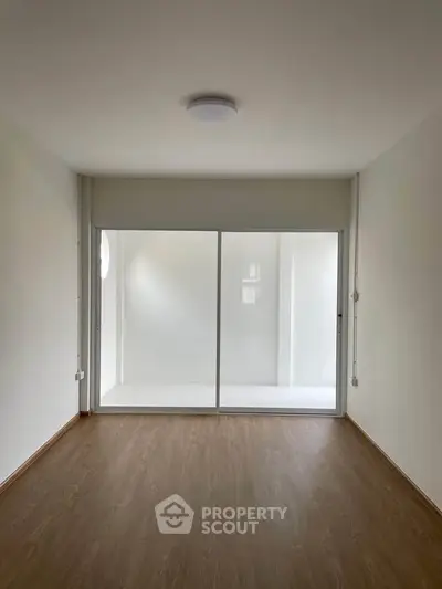 Spacious empty room with wooden flooring and large sliding glass doors leading to a bright balcony.