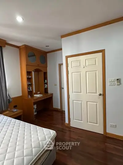 Spacious bedroom with wooden accents and natural light, featuring a cozy workspace and comfortable mattress.