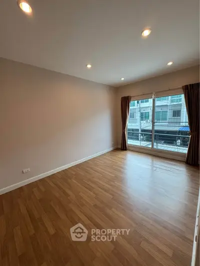 Spacious empty room with wooden flooring and large window, ideal for customization.