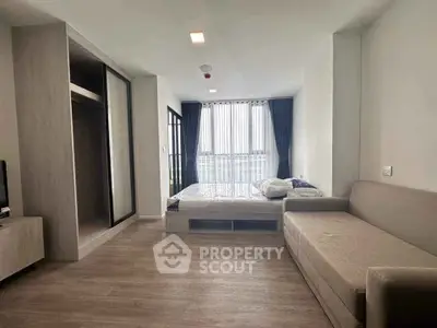 Modern studio apartment with cozy bed and stylish sofa, featuring large windows and elegant flooring.