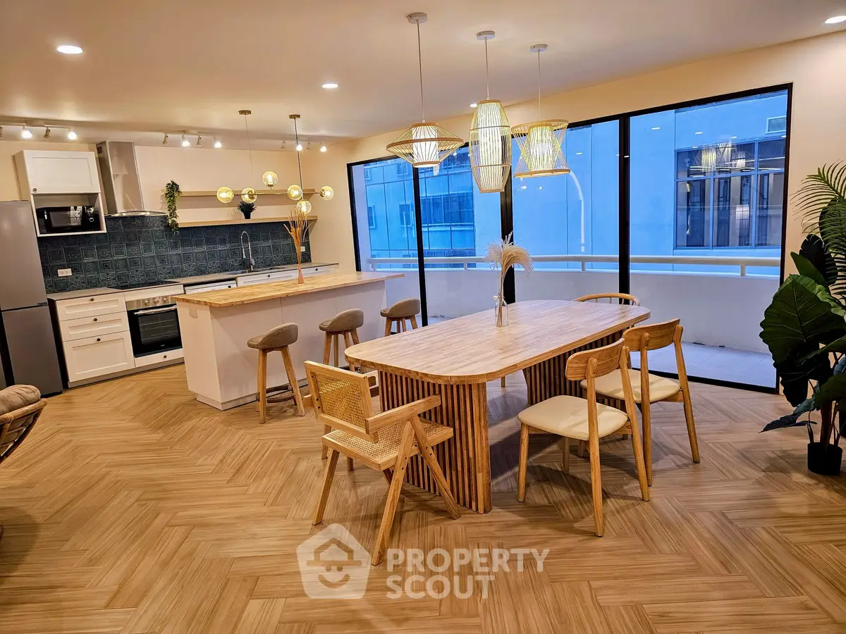 Modern kitchen with open layout and stylish dining area, featuring elegant lighting and large windows.