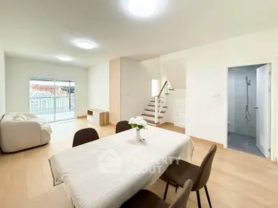 Spacious modern living room with dining area and staircase, featuring elegant decor and natural light.