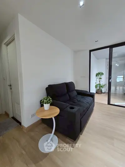 Modern living room with sleek black sofa and stylish side table, featuring wooden flooring and glass door.