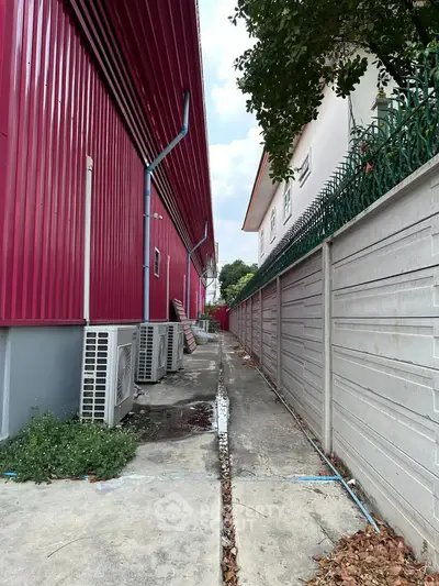 Narrow alley between vibrant red building and white house with lush greenery