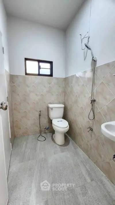 Modern bathroom with tiled walls and floor, featuring a toilet and shower area.