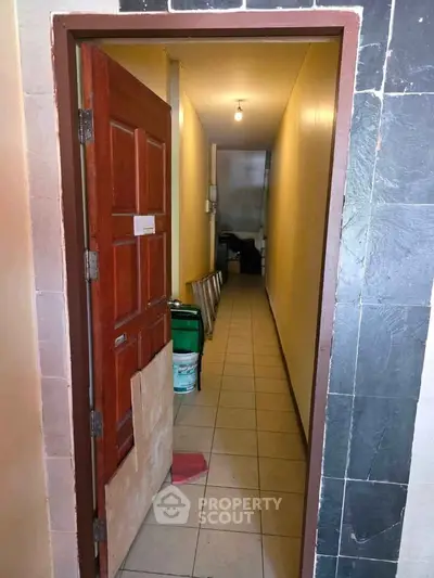 Narrow hallway with tiled floor and open wooden door, leading to storage area.