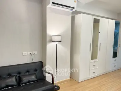 Modern living room with sleek black sofa, floor lamp, and white wardrobe in stylish apartment.
