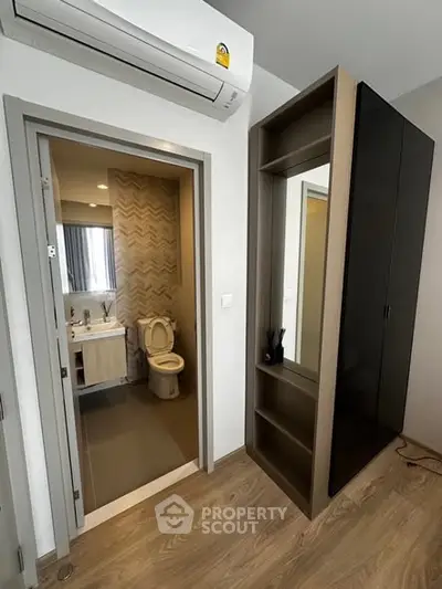 Modern apartment interior with bathroom and sleek storage unit, featuring wood flooring and air conditioning.