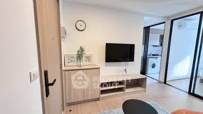 Modern living room with TV, wooden cabinet, and view into kitchen with washing machine.
