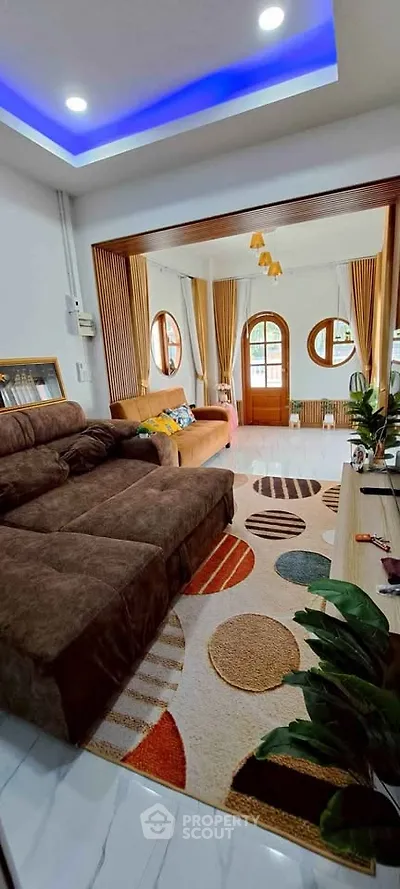 Spacious living room with modern decor and cozy seating area, featuring stylish lighting and vibrant rug.