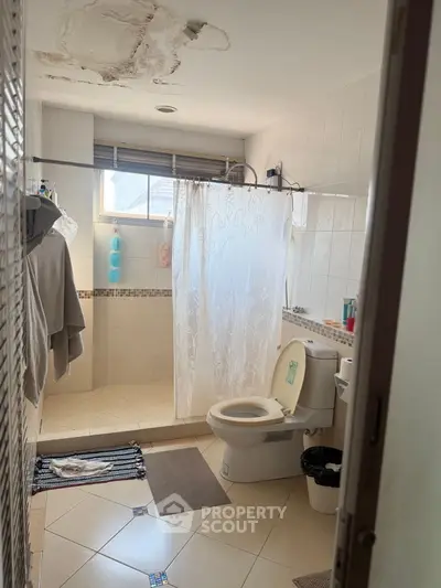 Spacious bathroom with natural light and tiled floor, featuring a shower and toilet.