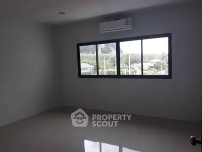 Spacious empty room with large window and air conditioning, offering a serene view of greenery outside.