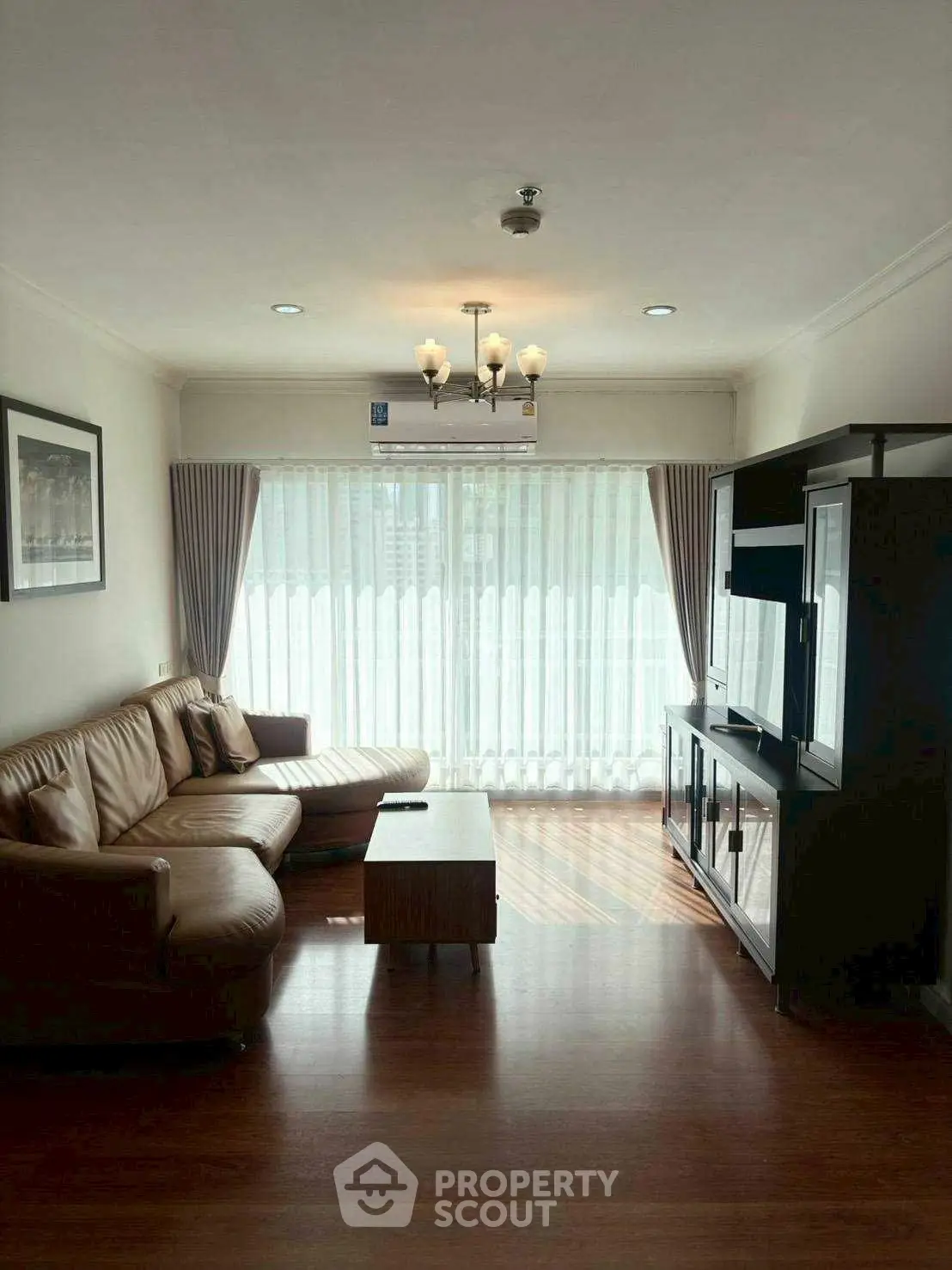Spacious living room with leather sofa and entertainment unit, featuring large windows and elegant lighting.