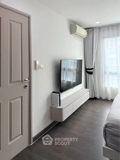 Modern bedroom with wall-mounted TV and air conditioning, featuring sleek design and natural light.