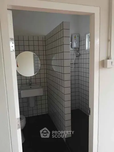 Compact bathroom with tiled walls and round mirror, featuring a shower and sink.