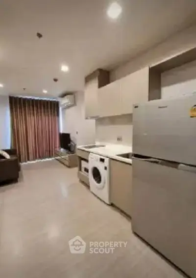 Modern open-layout kitchen with washing machine and fridge in cozy apartment.