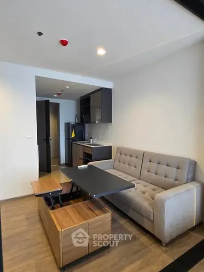 Modern living room with stylish sofa and compact kitchen area in open layout apartment.