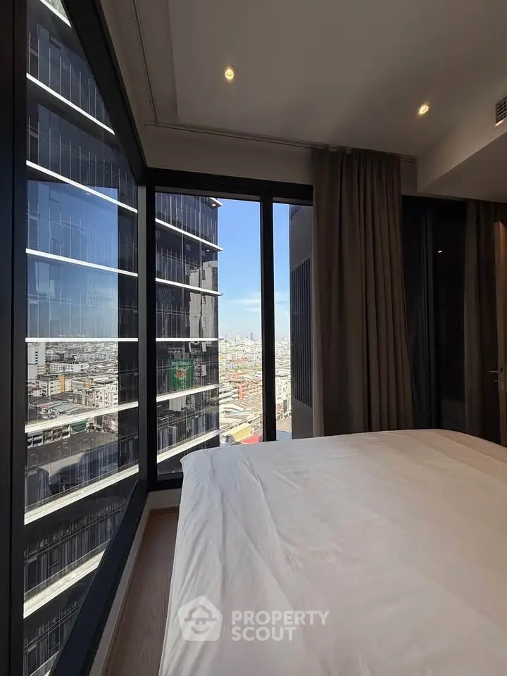 Modern bedroom with stunning city view from large windows in high-rise building.