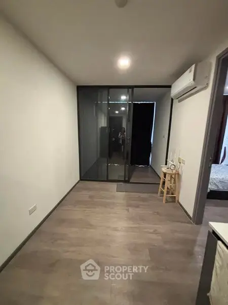 Modern apartment interior with sleek glass partition and wooden flooring.
