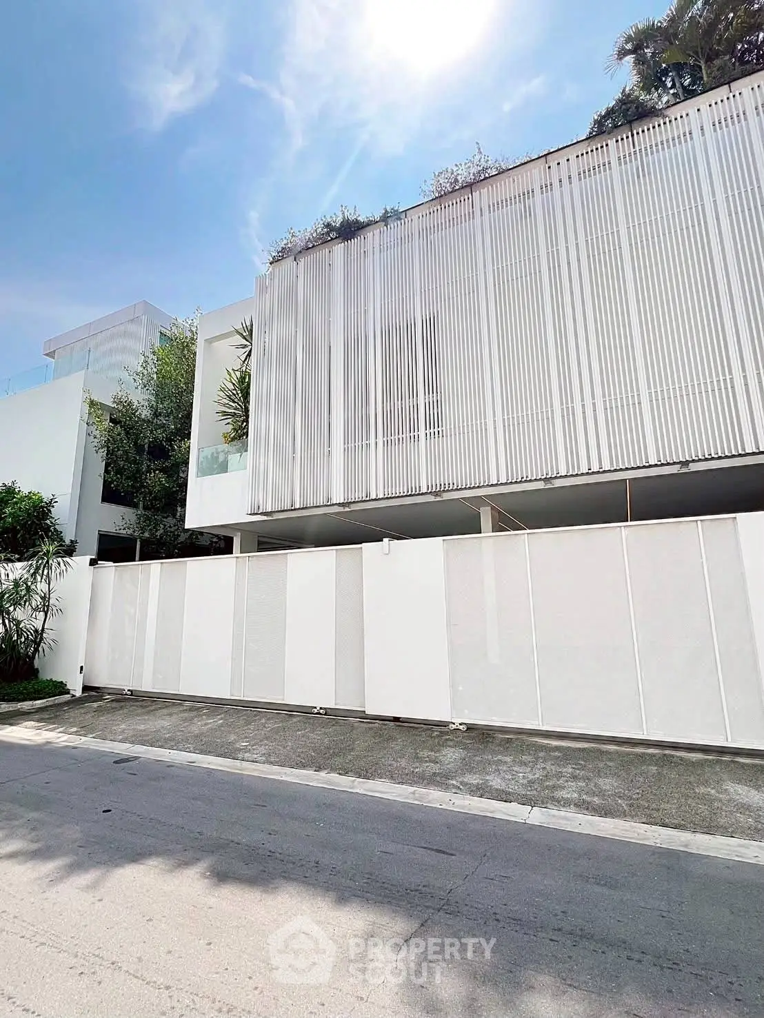 Modern minimalist white building exterior with sleek design and lush greenery.