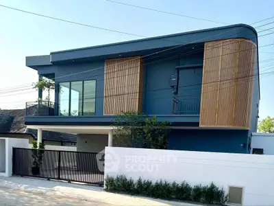 Modern two-story house with sleek design and wooden accents, featuring large windows and a gated entrance.
