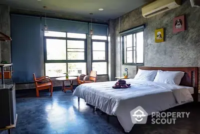 Spacious industrial-style bedroom with polished concrete walls, large windows offering ample natural light, and stylish vintage furniture.