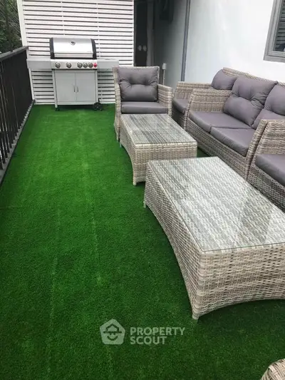 Stylish balcony with artificial grass, wicker furniture, and BBQ grill for outdoor relaxation.
