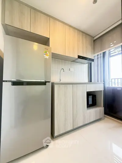 Modern kitchen with sleek cabinetry and stainless steel fridge in a bright apartment.