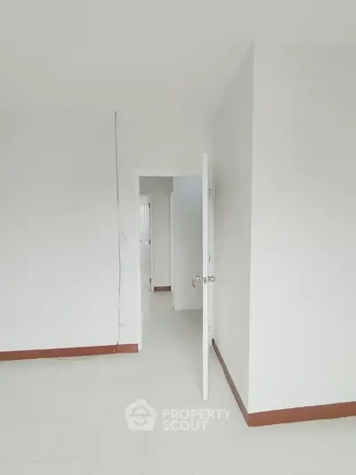 Minimalist interior with white walls and open door, showcasing potential living space.