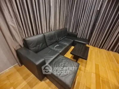 Luxurious black leather sectional sofa in a modern living room with elegant wooden flooring and stylish curtains.