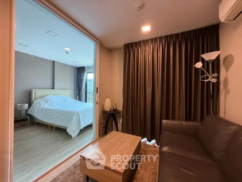 Modern apartment with cozy living room and bedroom separated by glass wall, featuring stylish furniture.
