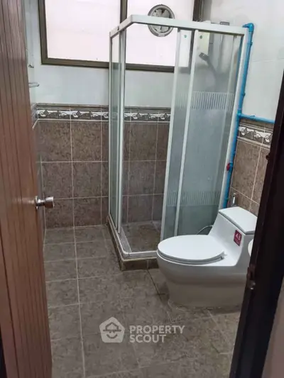 Compact bathroom with shower enclosure and modern toilet in tiled interior.