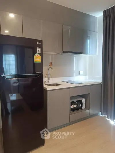 Modern kitchen with sleek cabinetry and black fridge in a stylish apartment.