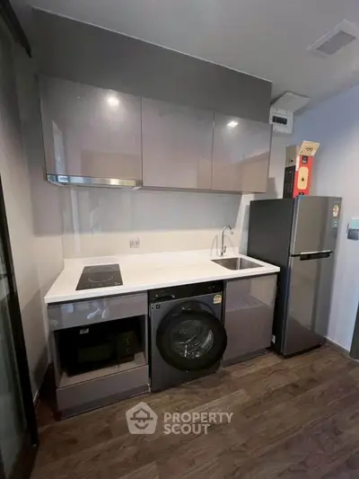 Modern compact kitchen with sleek cabinets, washing machine, and fridge in a stylish apartment.