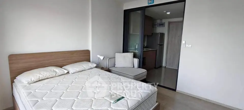 Modern bedroom with cozy bed and view into compact kitchen area.