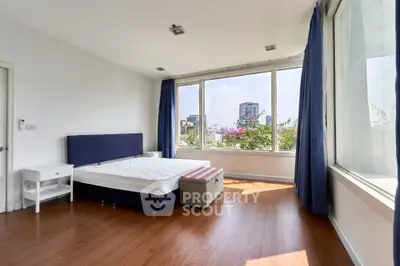 Spacious bedroom with large windows and city view, featuring modern decor and wooden flooring.