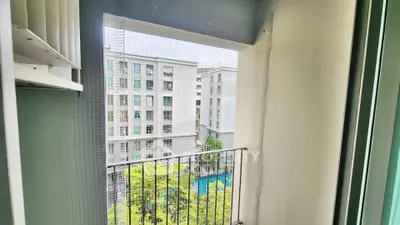 Charming balcony view overlooking modern apartment complex with lush greenery and pool.