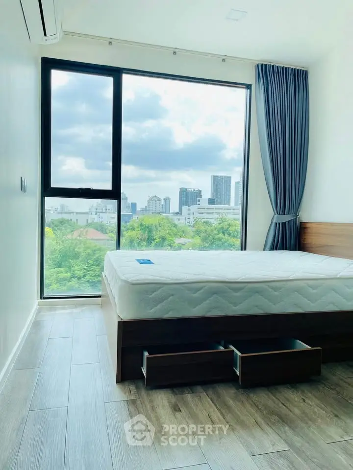 Modern bedroom with large window offering stunning city view and ample natural light.