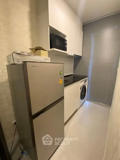 Modern kitchen with sleek appliances and compact design, featuring a fridge, microwave, and washing machine.