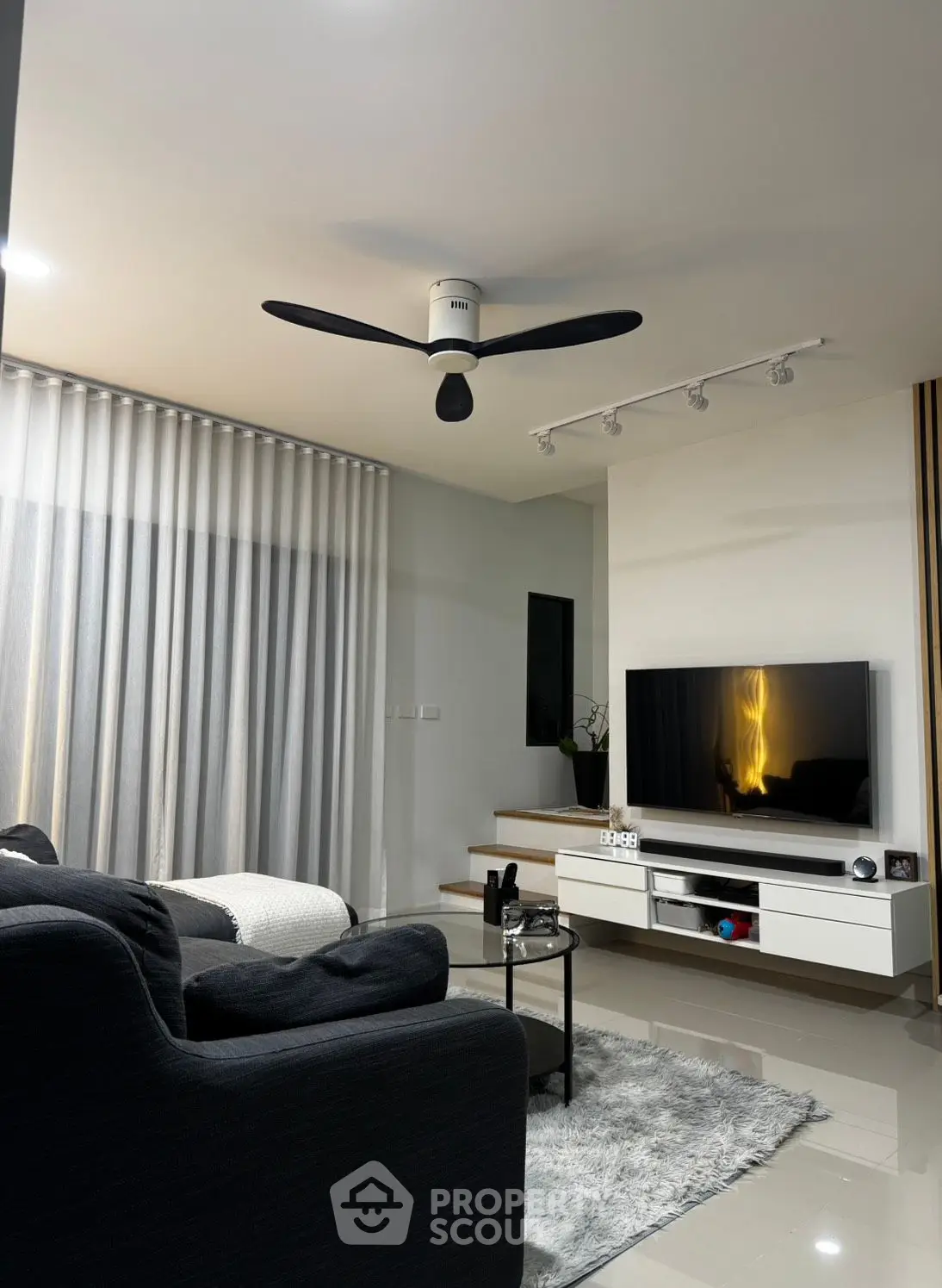 Modern living room with sleek furniture, large TV, and ceiling fan, perfect for relaxation and entertainment.