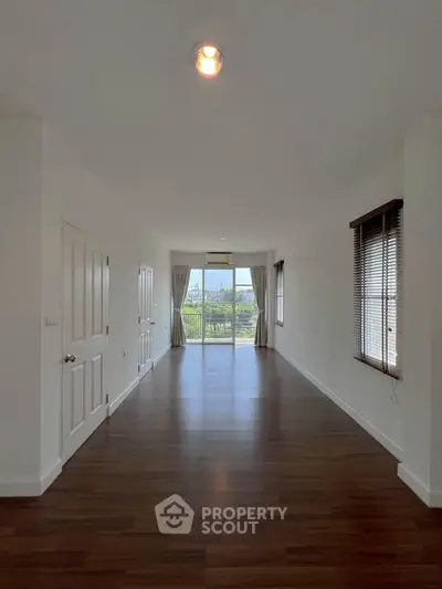 Spacious empty room with wooden flooring and large windows offering natural light and scenic views.