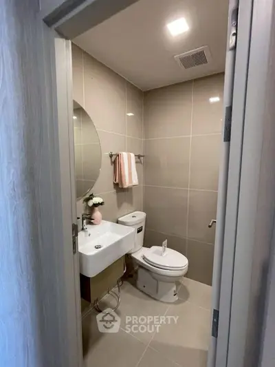Modern bathroom with sleek fixtures and neutral tiles, featuring a round mirror and stylish decor.