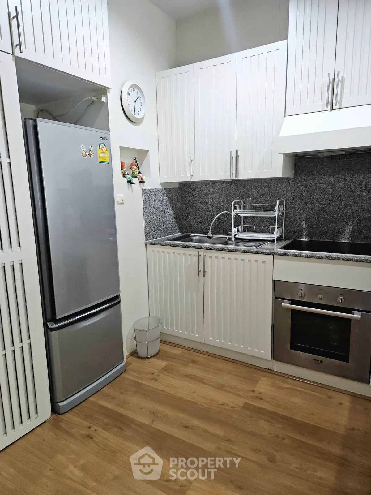 Modern kitchen with sleek white cabinets, stainless steel fridge, and built-in oven in a cozy apartment.