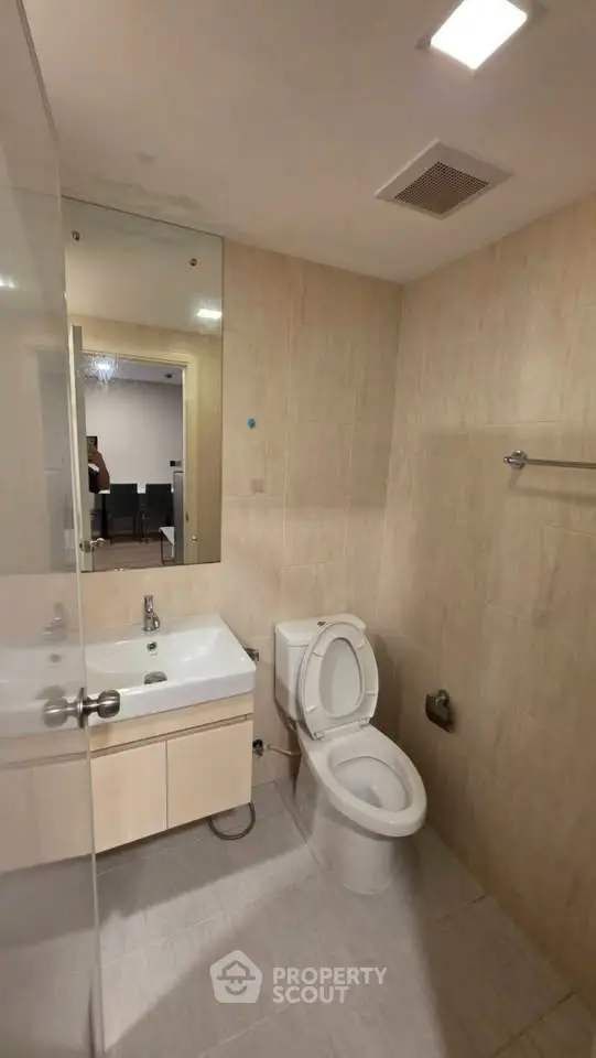 Modern bathroom with sleek fixtures and neutral tiles, featuring a large mirror and compact vanity unit.