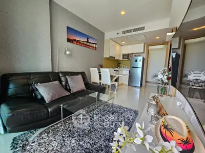 Modern living room with sleek black sofa, glass coffee table, and stylish kitchen area.
