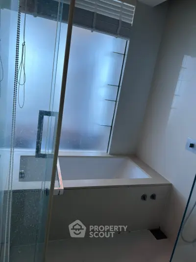 Modern bathroom with sleek bathtub and frosted glass window for privacy.
