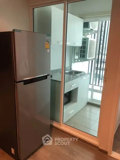 Modern kitchen with sleek refrigerator and glass sliding door leading to balcony.