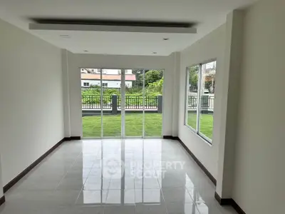Spacious living room with large windows offering a lush garden view, perfect for natural light lovers.